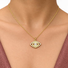 Load image into Gallery viewer, A gold chain necklace with an evil eye pendant worn by a person, shown from the chest up against a brick wall background.