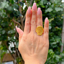 Load image into Gallery viewer, Hand wearing a gold shell-shaped ring with a green leafy background

